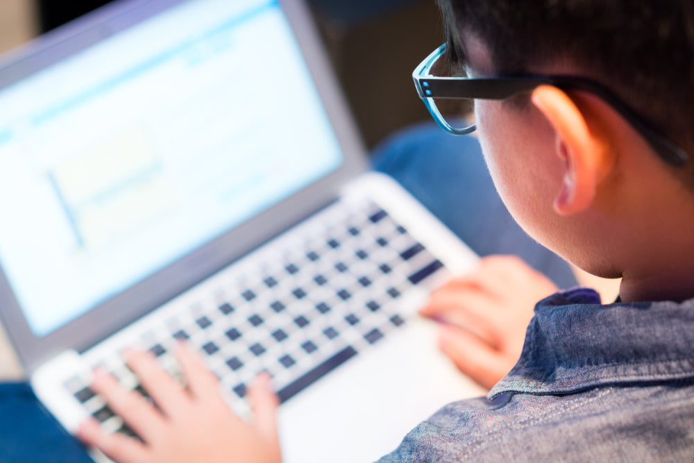 Preteen boy with blue light blocking glasses is online learning with his laptop. 