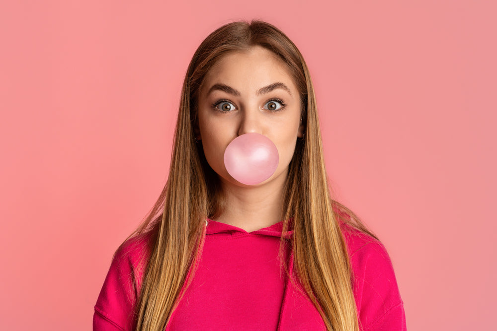 Bubble from chewing gum. Teenage girl on pink background