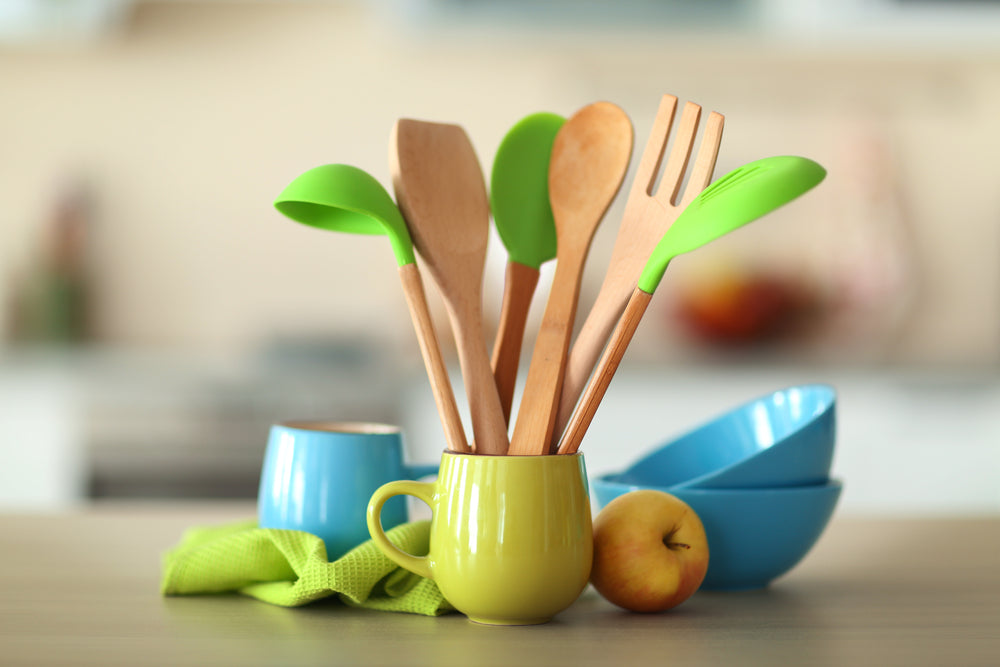 Set of wooden kitchen utensils in green cup with napkin and dishes on the table